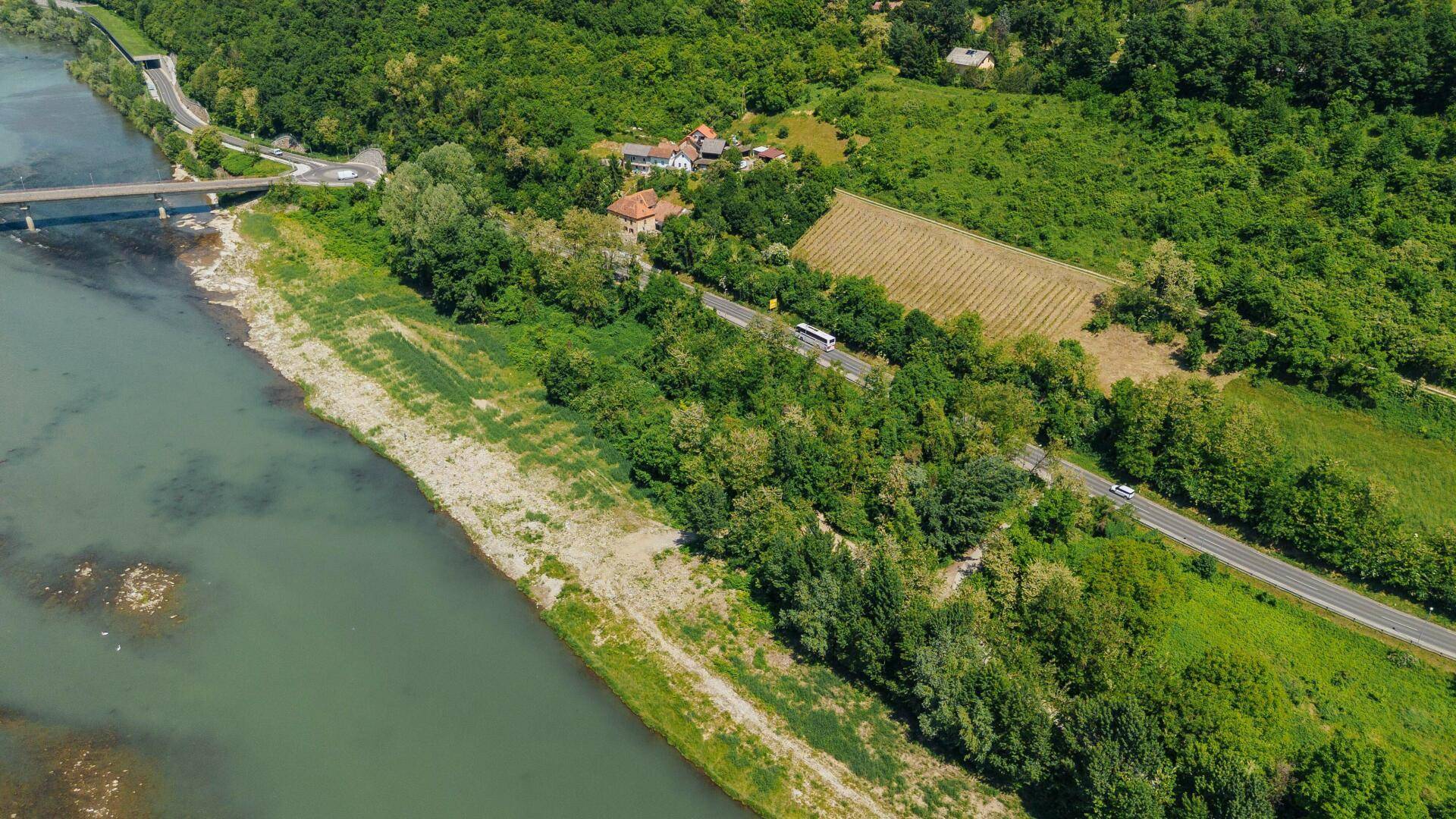 Luftaufnahme einer Flusslandschaft mit Straße, fahrenden Autos, grünen Hügeln und einem Weinberg.