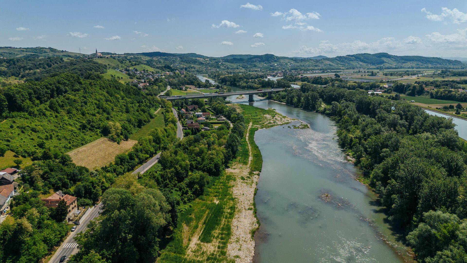 Luftaufnahme einer idyllischen grünen Landschaft mit Fluss, Brücke und ländlichen Siedlungen.