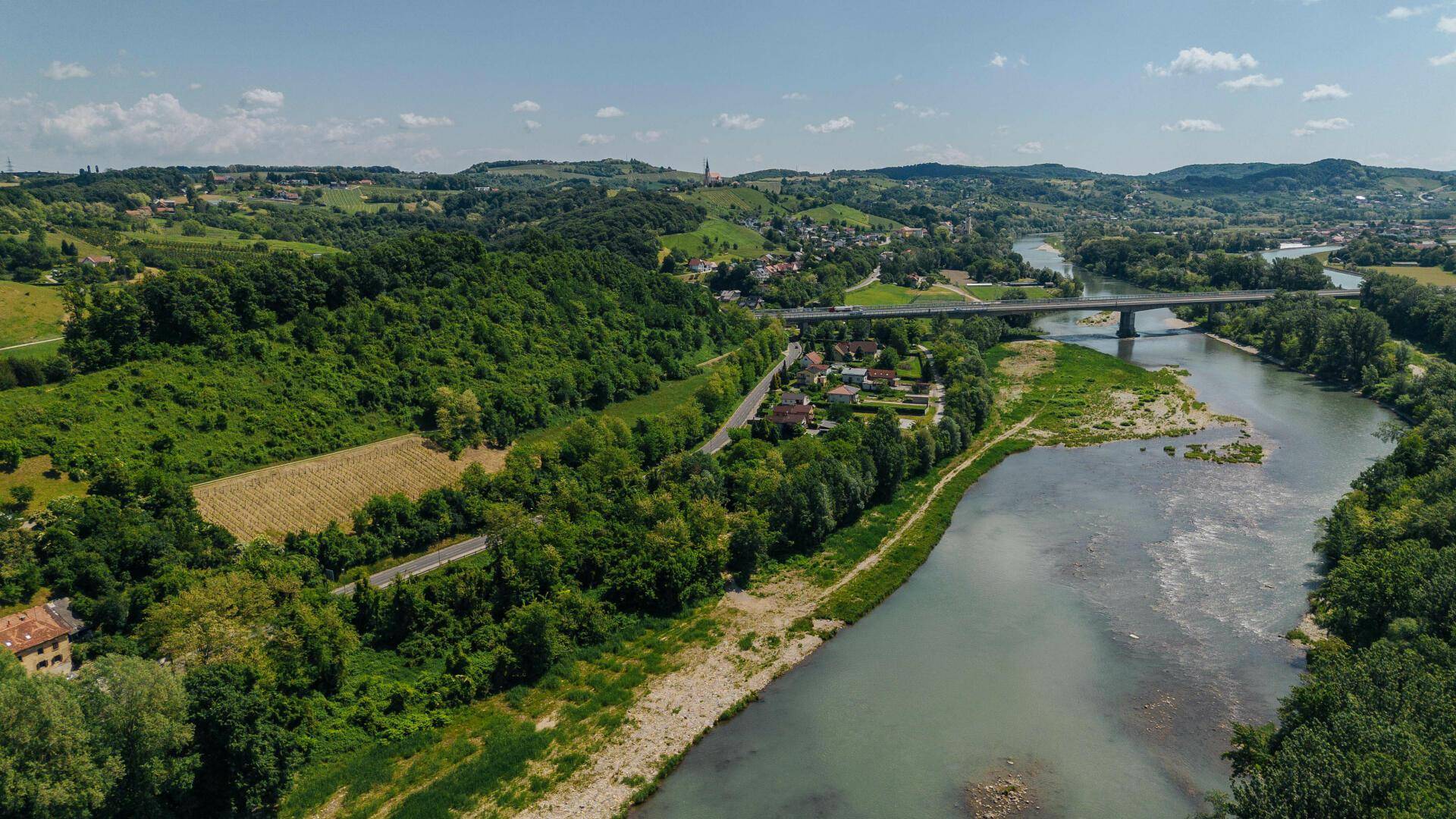 Weitläufige Ansicht einer grünen Landschaft mit Fluss, Brücke, Straße und ländlicher Bebauung.