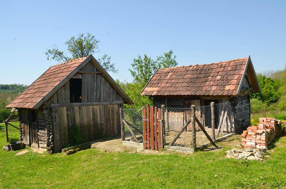 Zwei rustikale Holzschuppen oder Nebengebäude mit Ziegeldächern auf einem grünen Grundstück.
