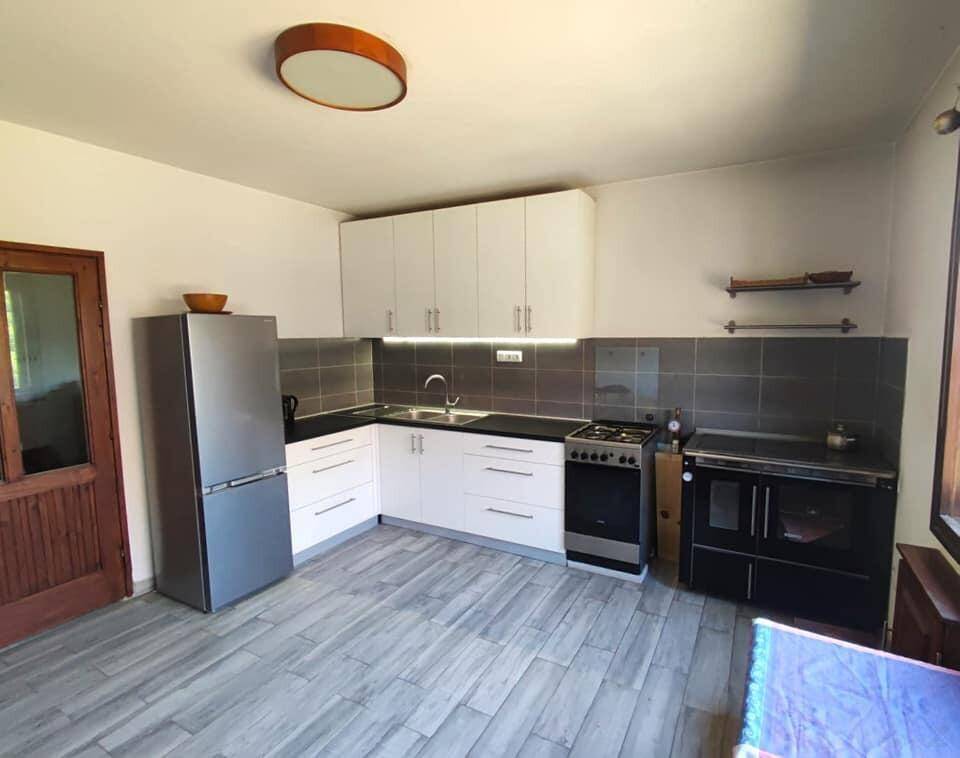 Funktionale Küche mit weißen Schränken, grauen Fliesen und einem freistehenden Kühlschrank sowie einem Holzofen.