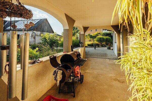 Überdachte Loggia mit Grillbereich und Blick auf den gepflasterten Hof und die Nebengebäude.