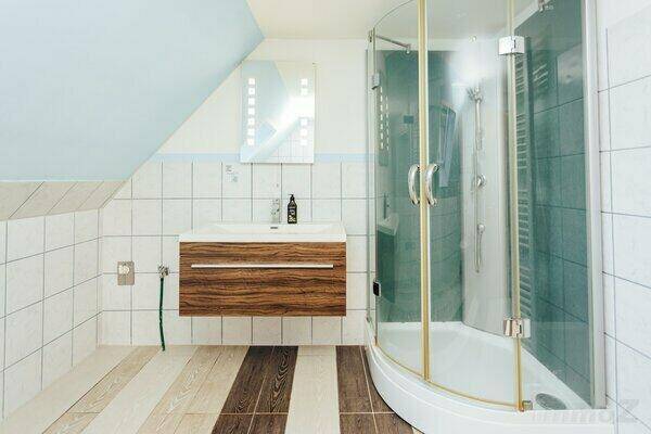 Modernes Badezimmer im Dachgeschoss mit Duschkabine, Holzwaschtisch und Fliesenboden.