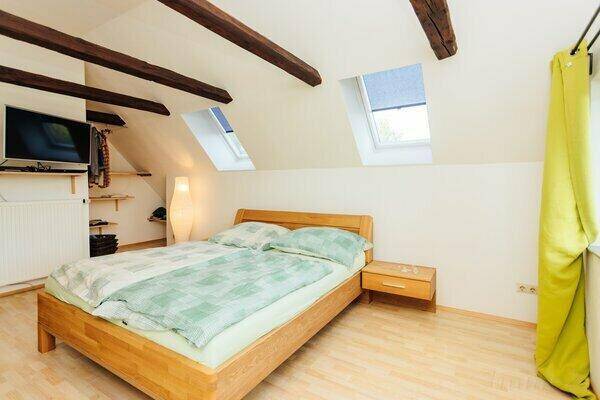 Helles Schlafzimmer mit Holzbalken, Holzbett und Dachfenstern, die den Raum erhellen.