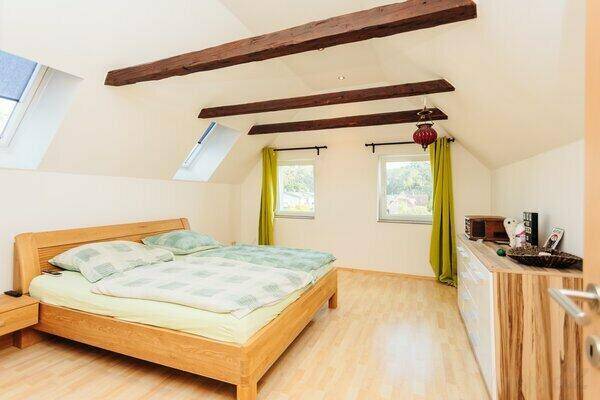 Schlafzimmer im Dachgeschoss mit Holzbalken, Holzbett und Dachfenstern für viel Licht.