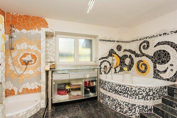 Badezimmer mit kreativer Mosaikgestaltung, Badewanne und Duschbereich mit Fenster.