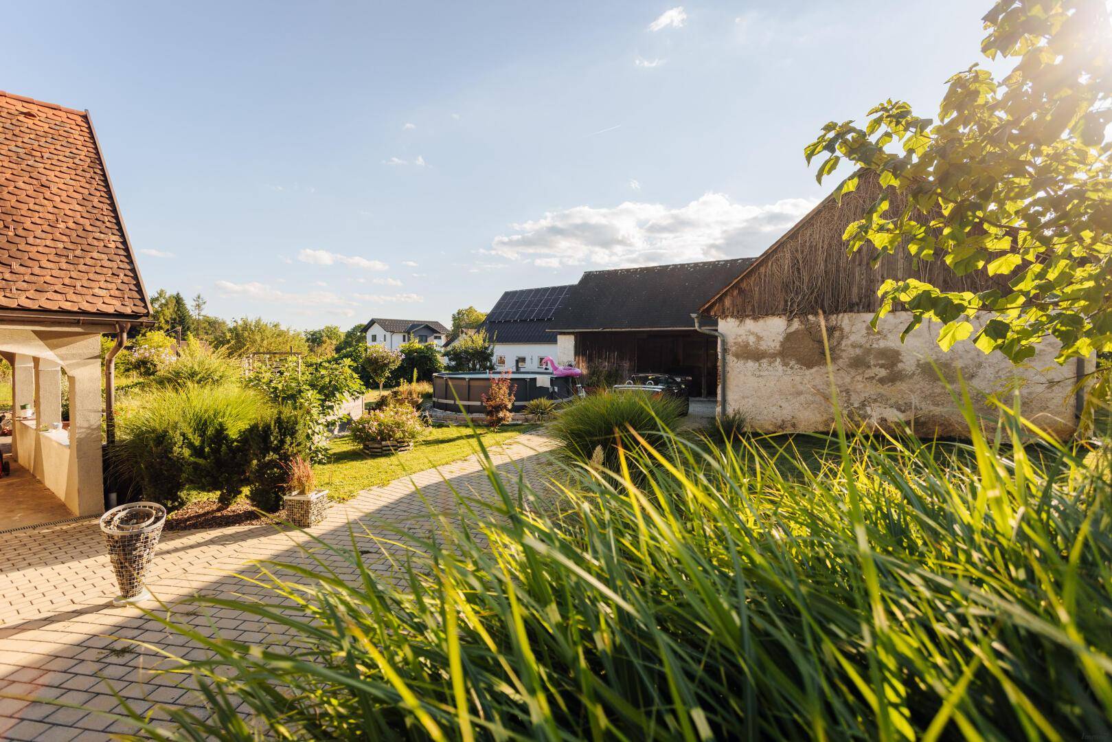Gepflasterter Weg und Gartenbereich mit Blick auf die Loggia und Nebengebäude.