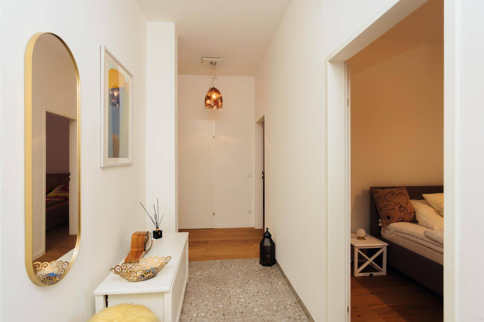 Schmaler Flur mit Spiegel und Blick in ein angrenzendes Schlafzimmer.