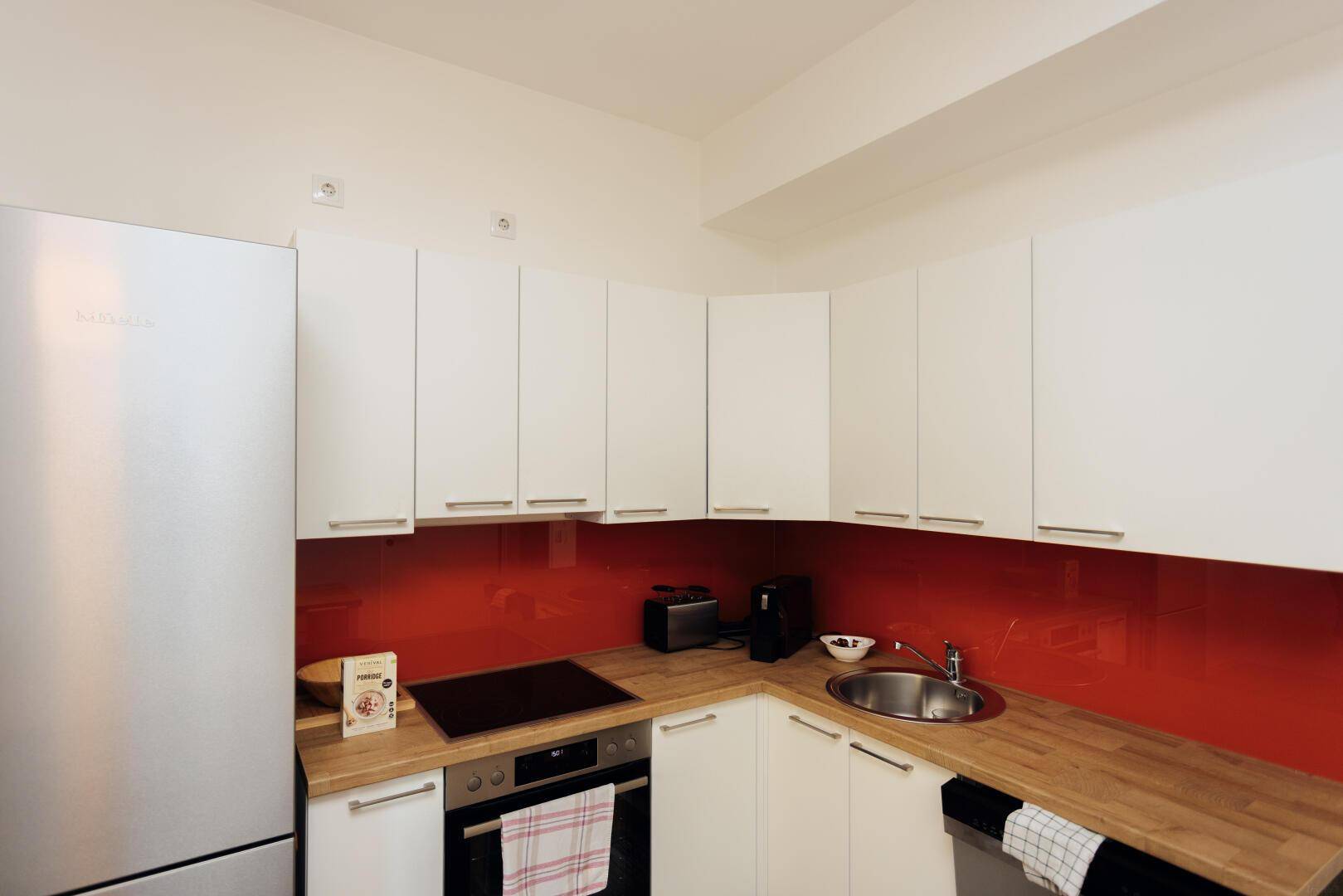 Moderne Küche mit weißen Schränken, roter Rückwand und Holzarbeitsplatte.