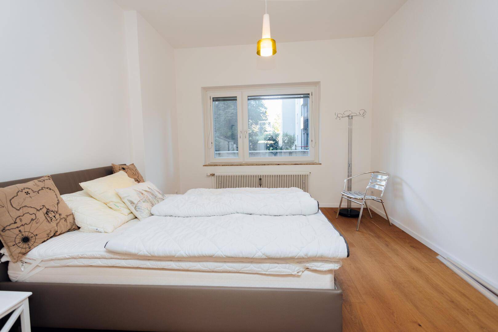 Helles Schlafzimmer mit Bett, Holzboden und großem Fenster.