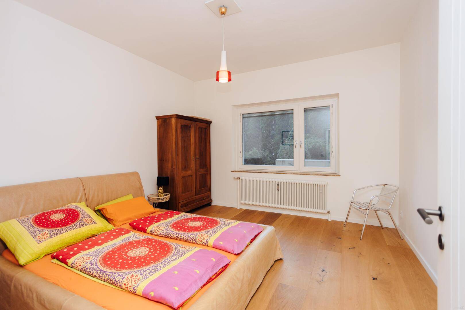 Schlafzimmer mit Doppelbett, Holzschrank und Fenster mit Blick ins Grüne.