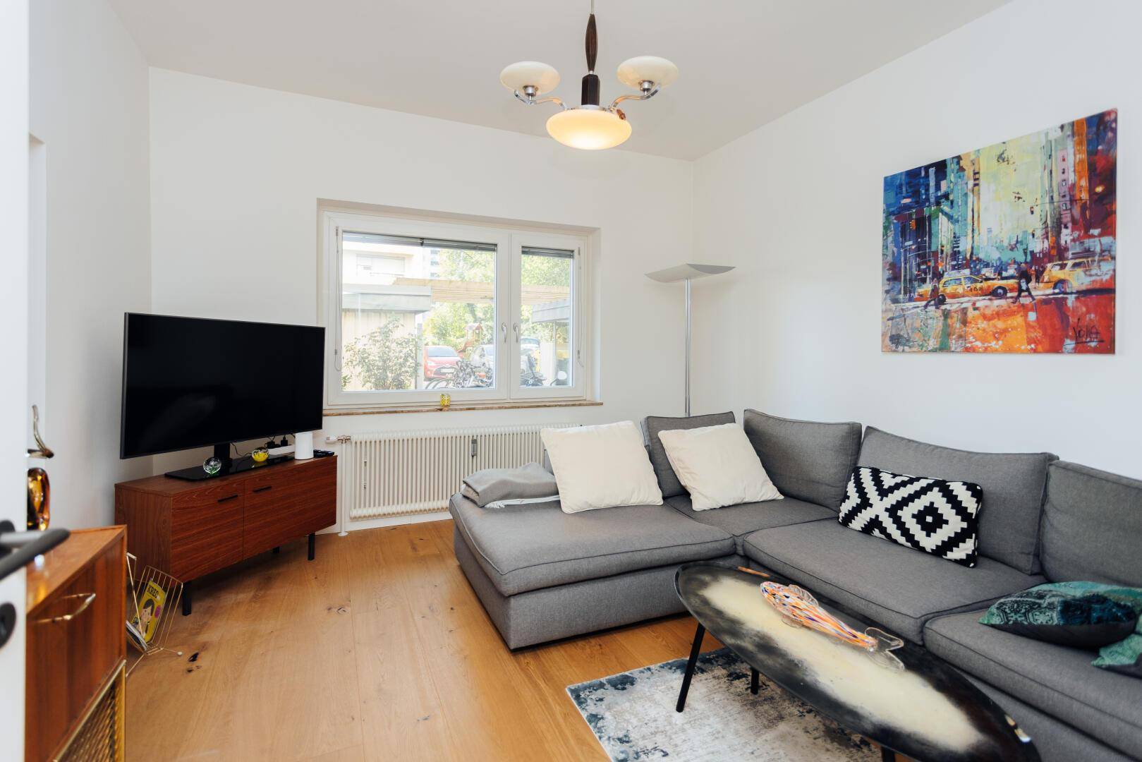 Gemütliches Wohnzimmer mit grauem Ecksofa, Fernseher und Holzboden.