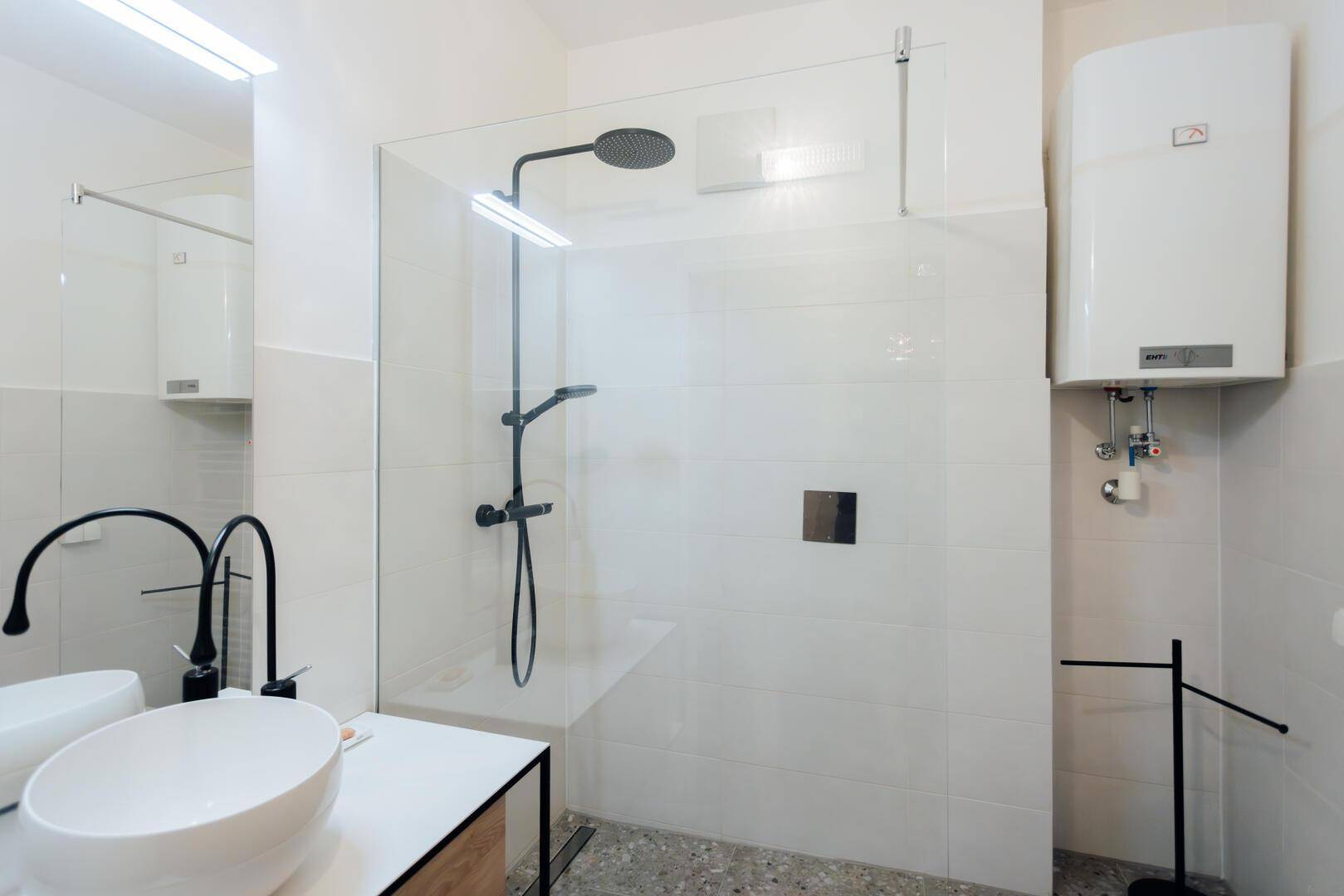 Helles Badezimmer mit großer Duschkabine, weißer Fliesenwand und modernem Waschbecken.