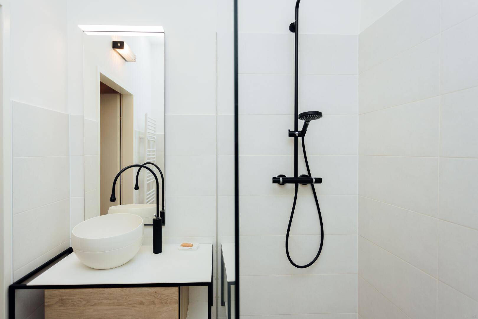 Modernes Badezimmer mit weißer Fliesenwand, schwarzer Armatur und Duschbereich.