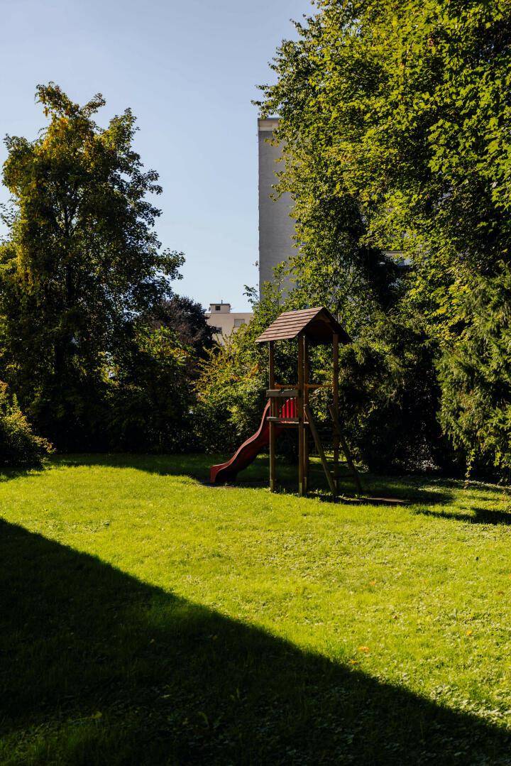 Grüner Gartenbereich mit Rutsche und Bäumen, ideal für Kinder.