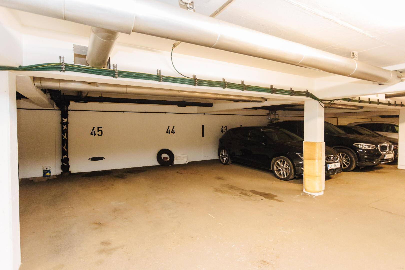 Tiefgarage mit mehreren Stellplätzen und sichtbaren Leitungen an der Decke.