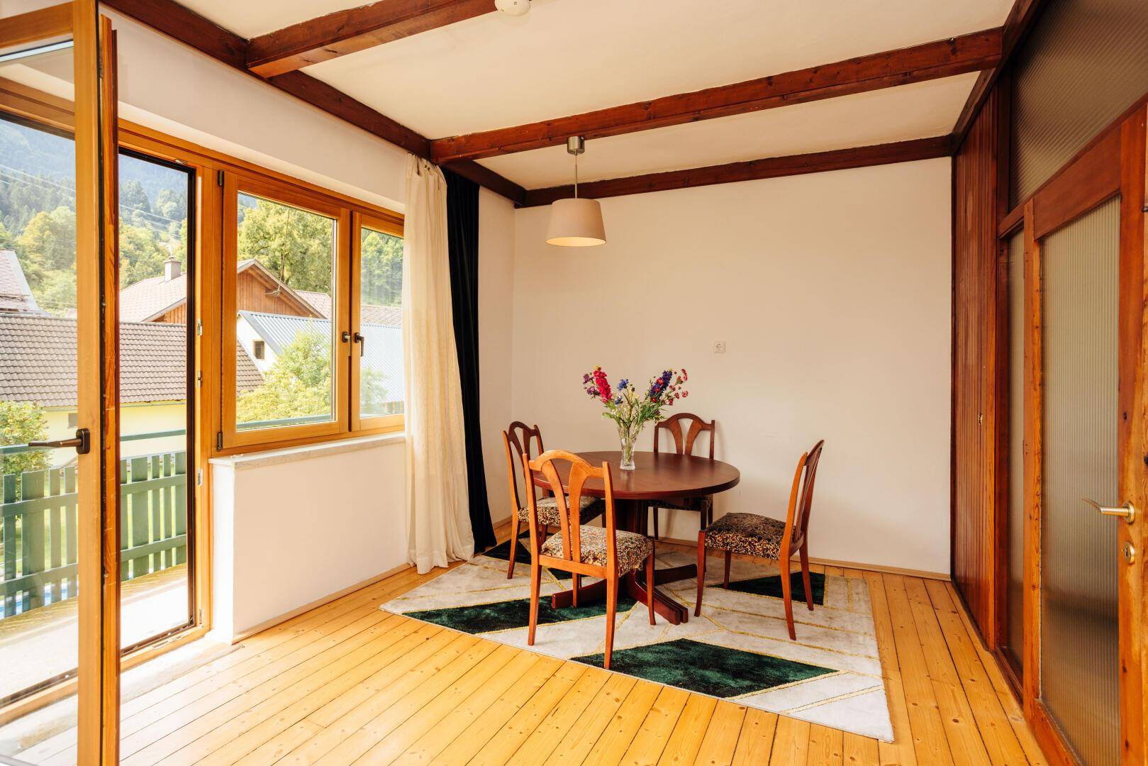 Gemütlicher Essbereich mit Holzboden, Holzbalken und Zugang zu einem Balkon mit grüner Aussicht.
