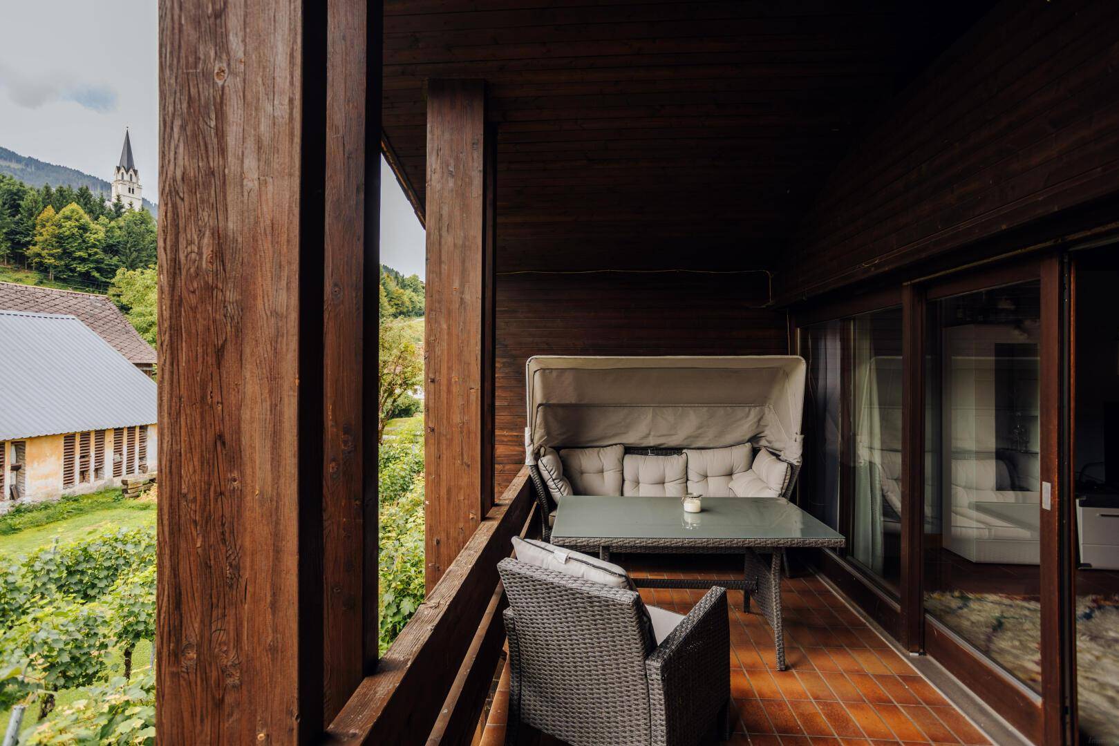 Überdachter Balkon mit Holzbalken, bequemen Gartenmöbeln und Blick auf die Umgebung.