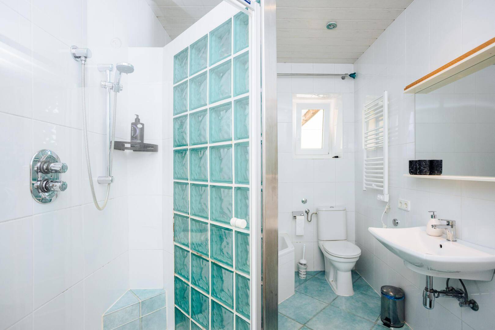 Badezimmer mit Duschkabine aus Glasbausteinen, WC, Waschbecken und beheiztem Handtuchhalter.