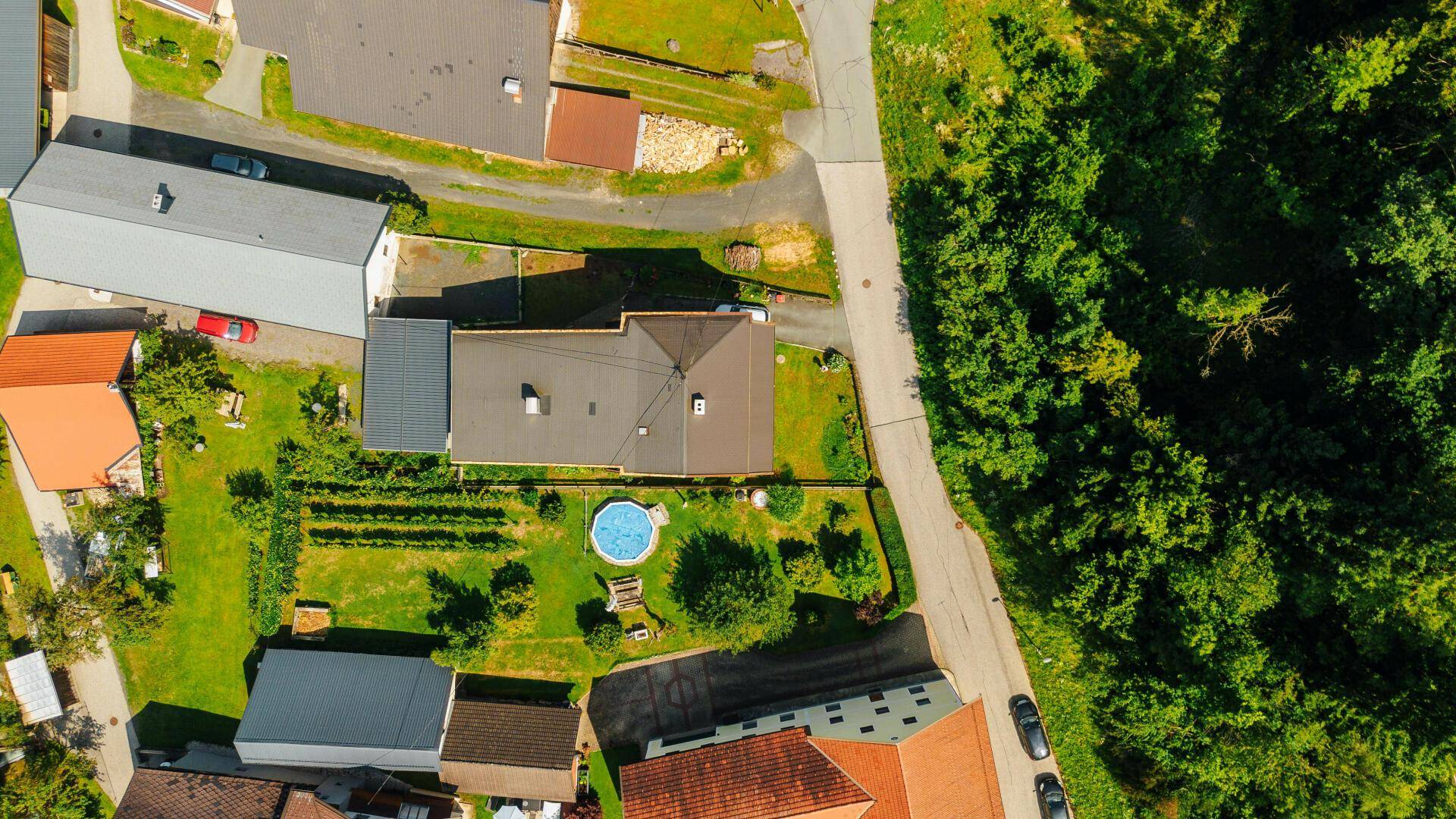 Draufsicht des Anwesens mit Haus, Garten, kleinem Pool und angrenzendem Waldgebiet und Weinberg.