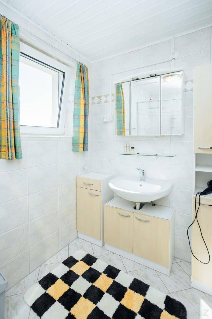 Helles Badezimmer mit weißen Fliesen, einem Waschbecken, Spiegelschrank und einem Fenster für Tageslicht.