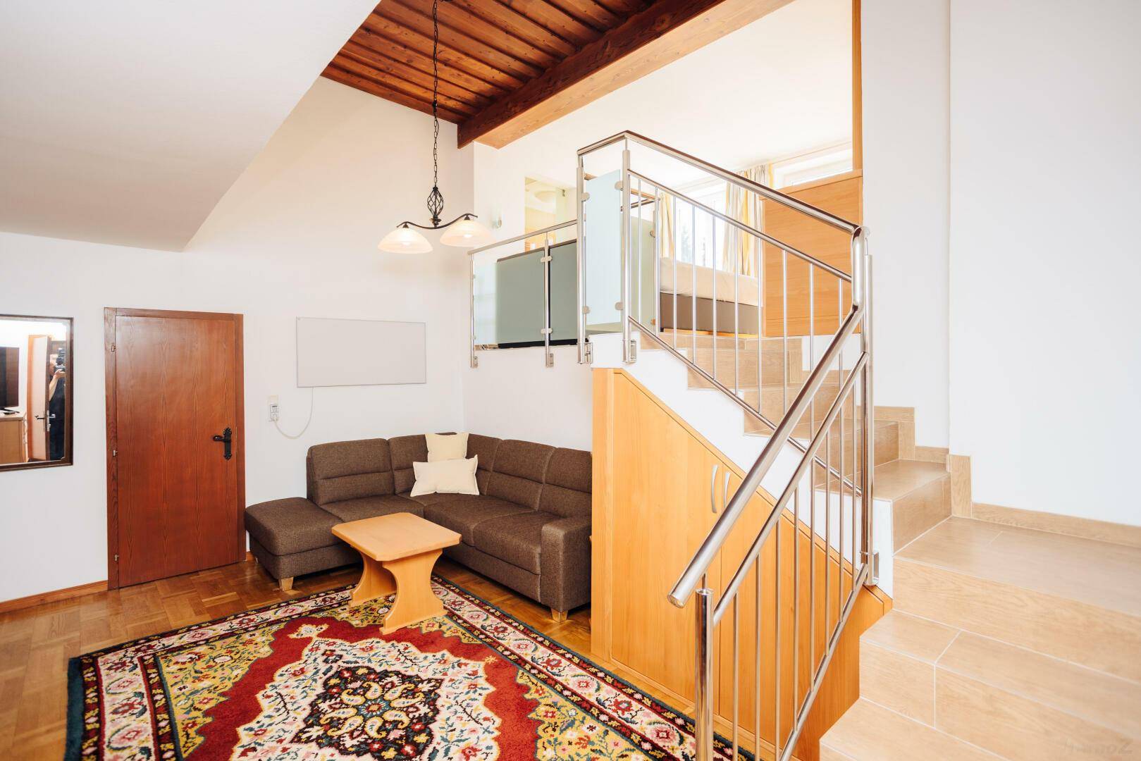 Gemütliches Wohnzimmer mit Holzbalkendecke, bequemer Couch und einer Treppe zum oberen Bereich.