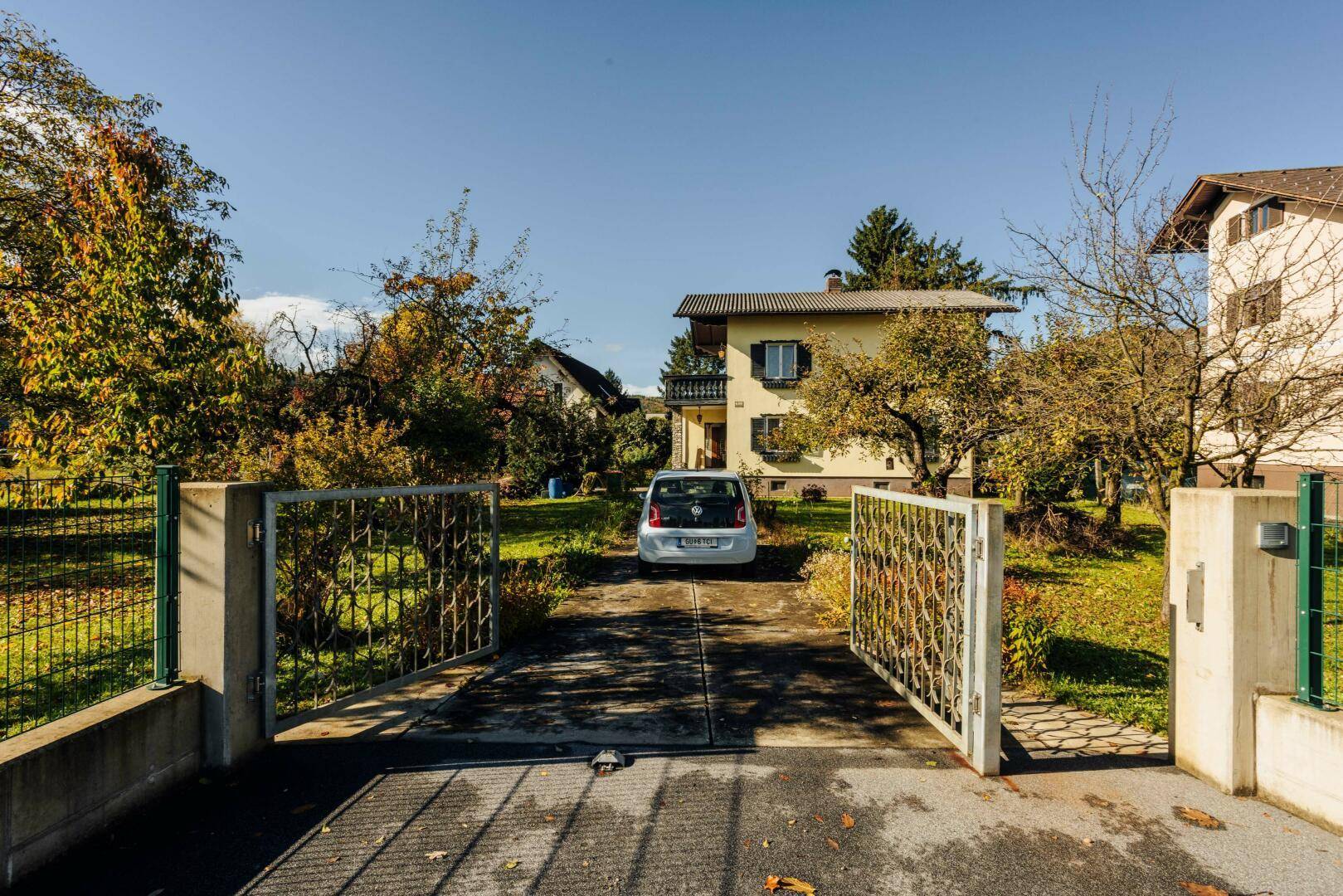 Offenes Eingangstor zur Zufahrt des Hauses mit geparktem Auto und umgebender Grünfläche.