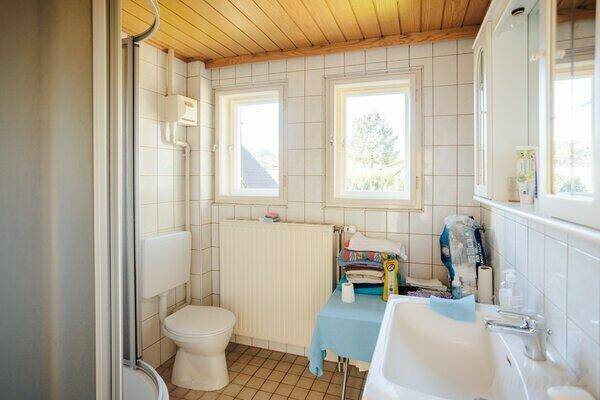 Badezimmer mit Duschkabine, WC, Waschbecken und zwei Fenstern für Tageslicht.