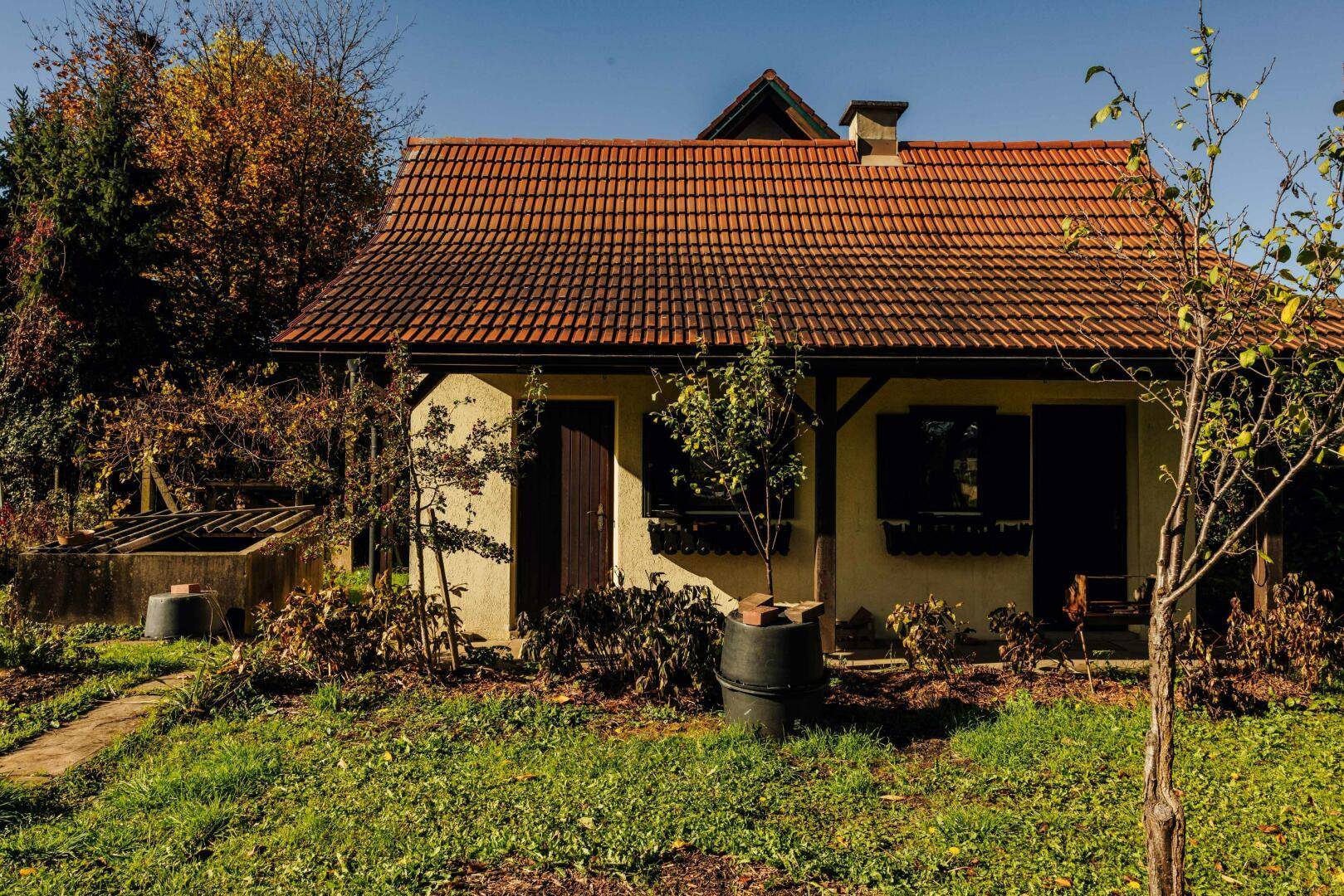 Kleines Nebengebäude mit Ziegeldach und Fensterläden im Gartenbereich.