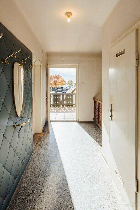 Langer Flur mit Terrazzoboden und Zugang zu einem Balkon, hell beleuchtet durch Tageslicht.