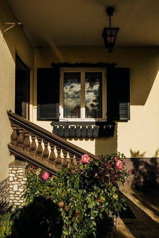 Eingangsbereich mit Steintreppe, schmiedeeisernem Geländer und einem Fenster mit Fensterläden.