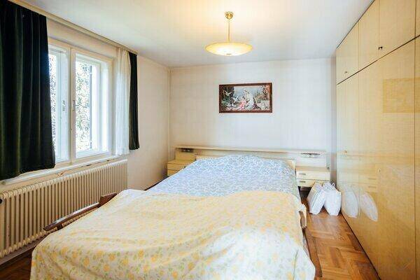 Schlafzimmer mit Parkettboden, Doppelbett und einem großen Fenster, das viel Licht hereinlässt.