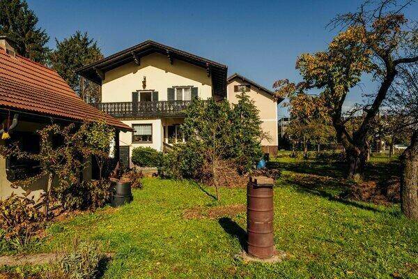 Rückansicht des Hauses mit Balkon und einem gepflegten Gartenbereich mit alten Bäumen.