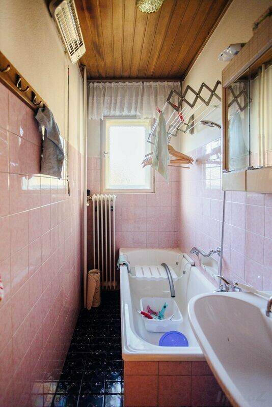 Badezimmer mit rosa Fliesen, Badewanne, Waschbecken und einem Fenster für natürliche Belüftung.