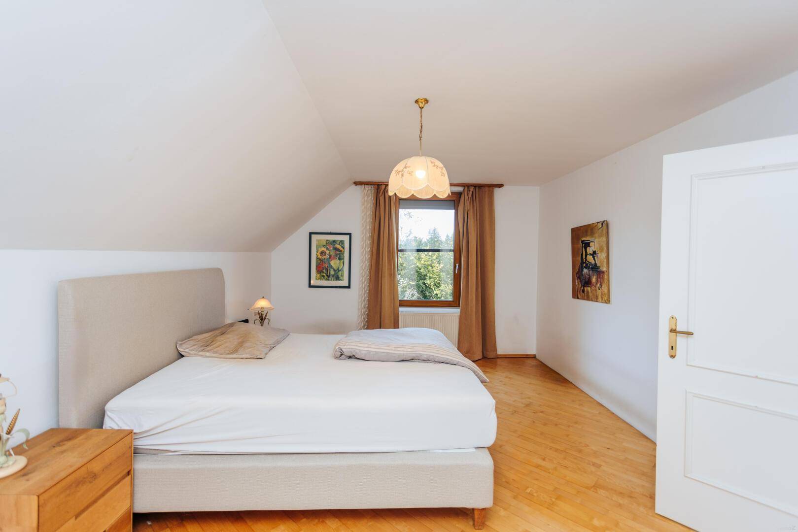Gemütliches Schlafzimmer mit Dachschräge, Parkettboden und Blick ins Grüne.