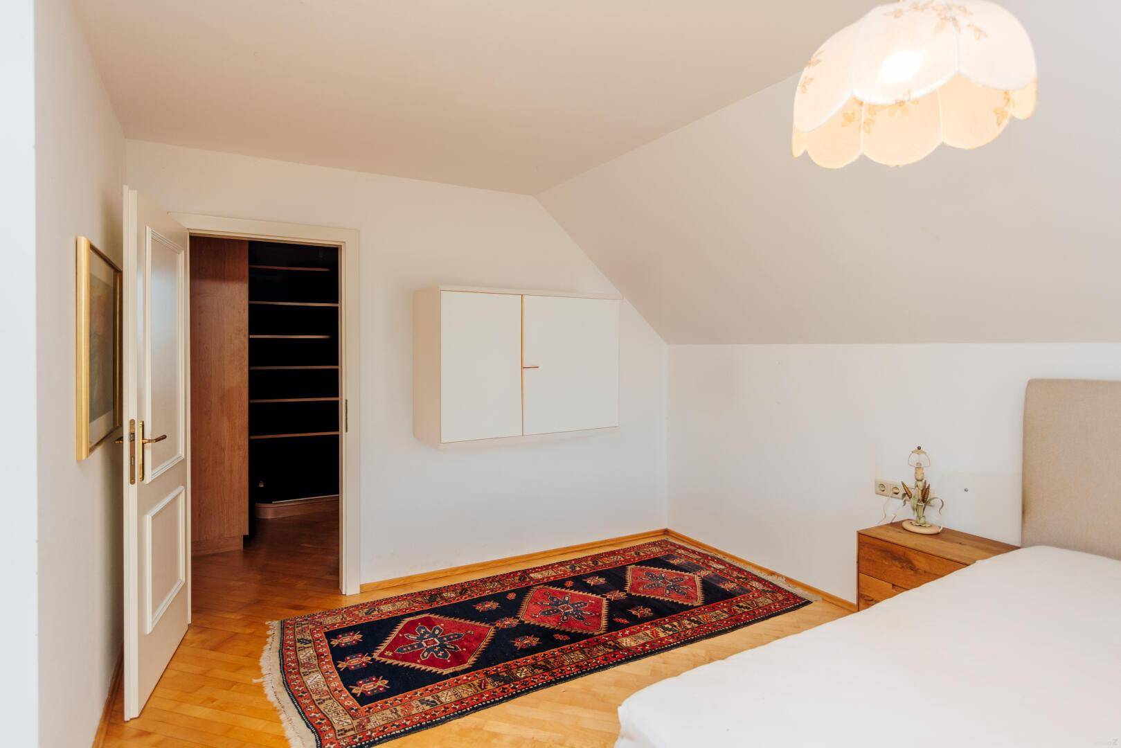 Schlafzimmer mit Parkettboden und Zugang zu einem begehbaren Kleiderschrank.
