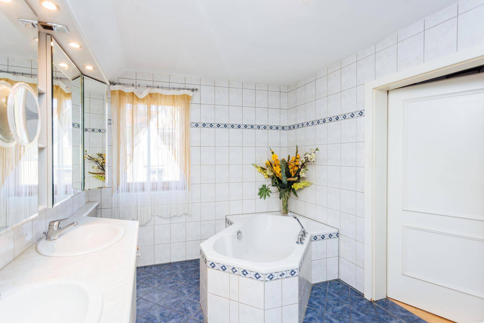 Geräumiges Badezimmer mit Doppelwaschbecken, Eckbadewanne und Fenster.