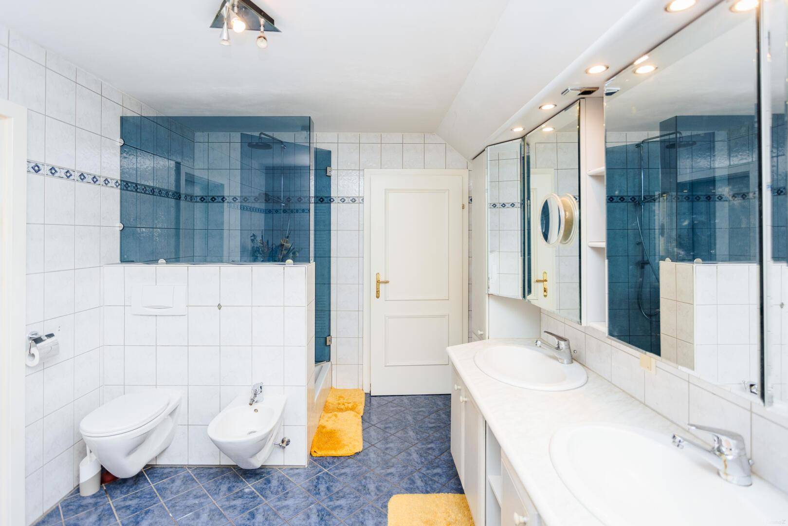 Geräumiges Badezimmer mit Doppelwaschbecken, Dusche, Bidet und blauen Fliesen.