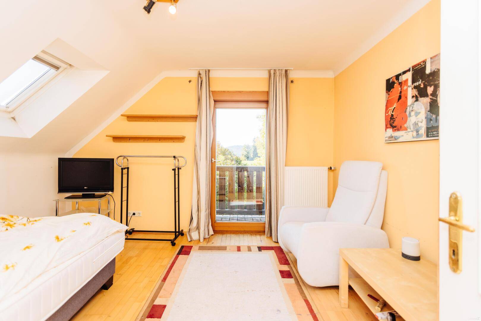 Helles Schlafzimmer mit Dachschräge, Balkonzugang und Blick in die Natur.