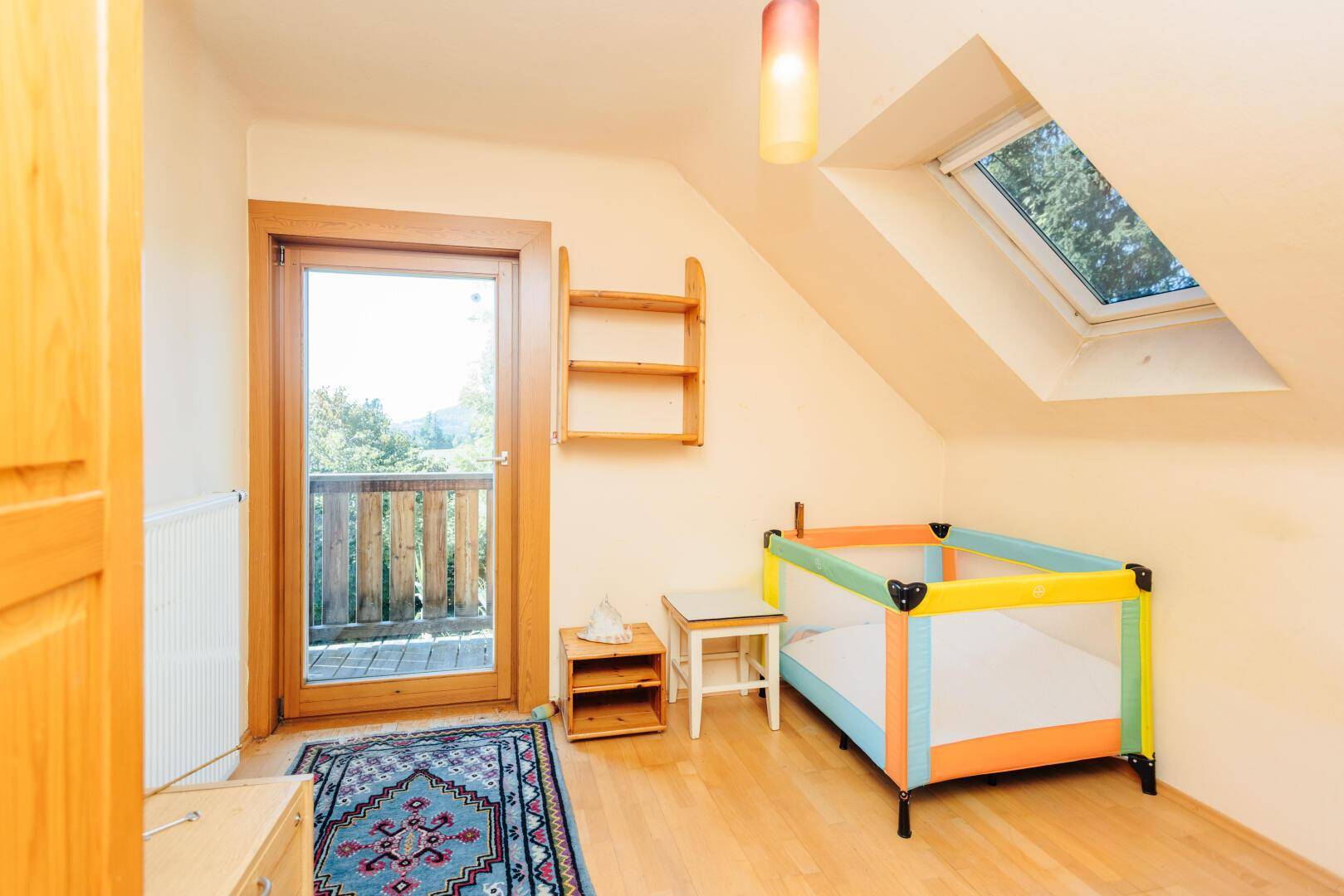 Kinderzimmer mit Holzboden, Babybett, Dachfenster und Zugang zum Balkon.