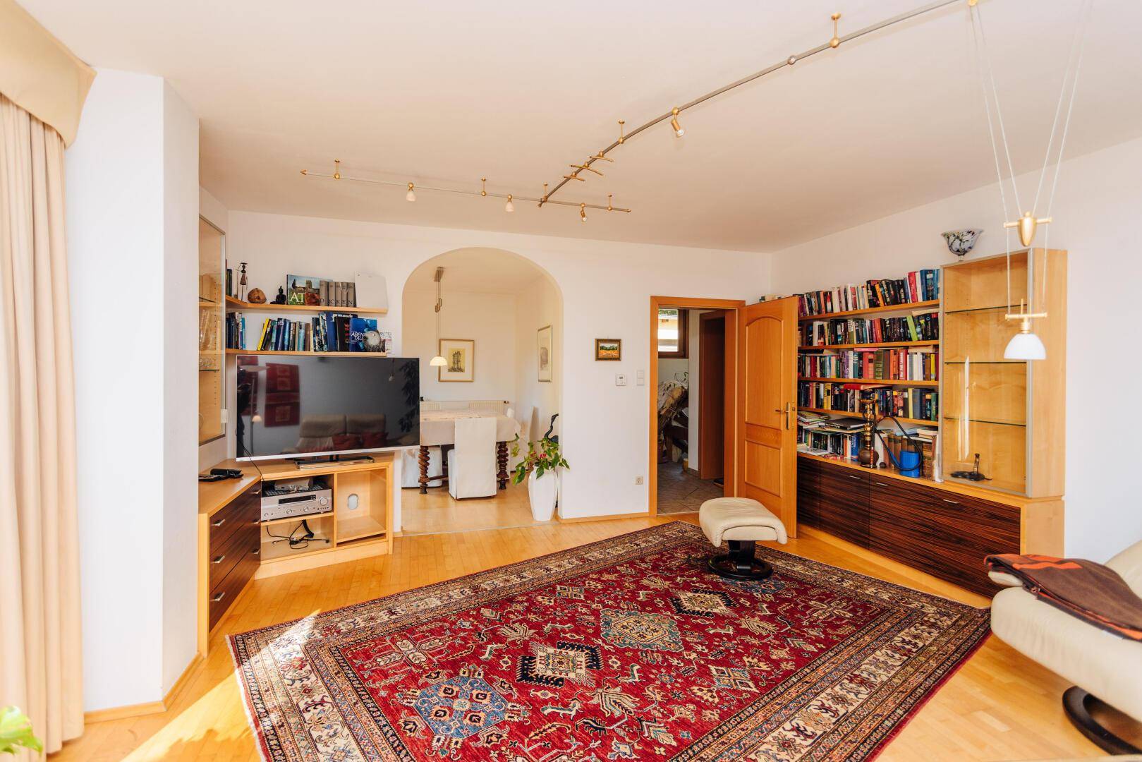 Geräumiges Wohnzimmer mit Parkettboden, Bücherregalen und einem Durchgang zum Essbereich.