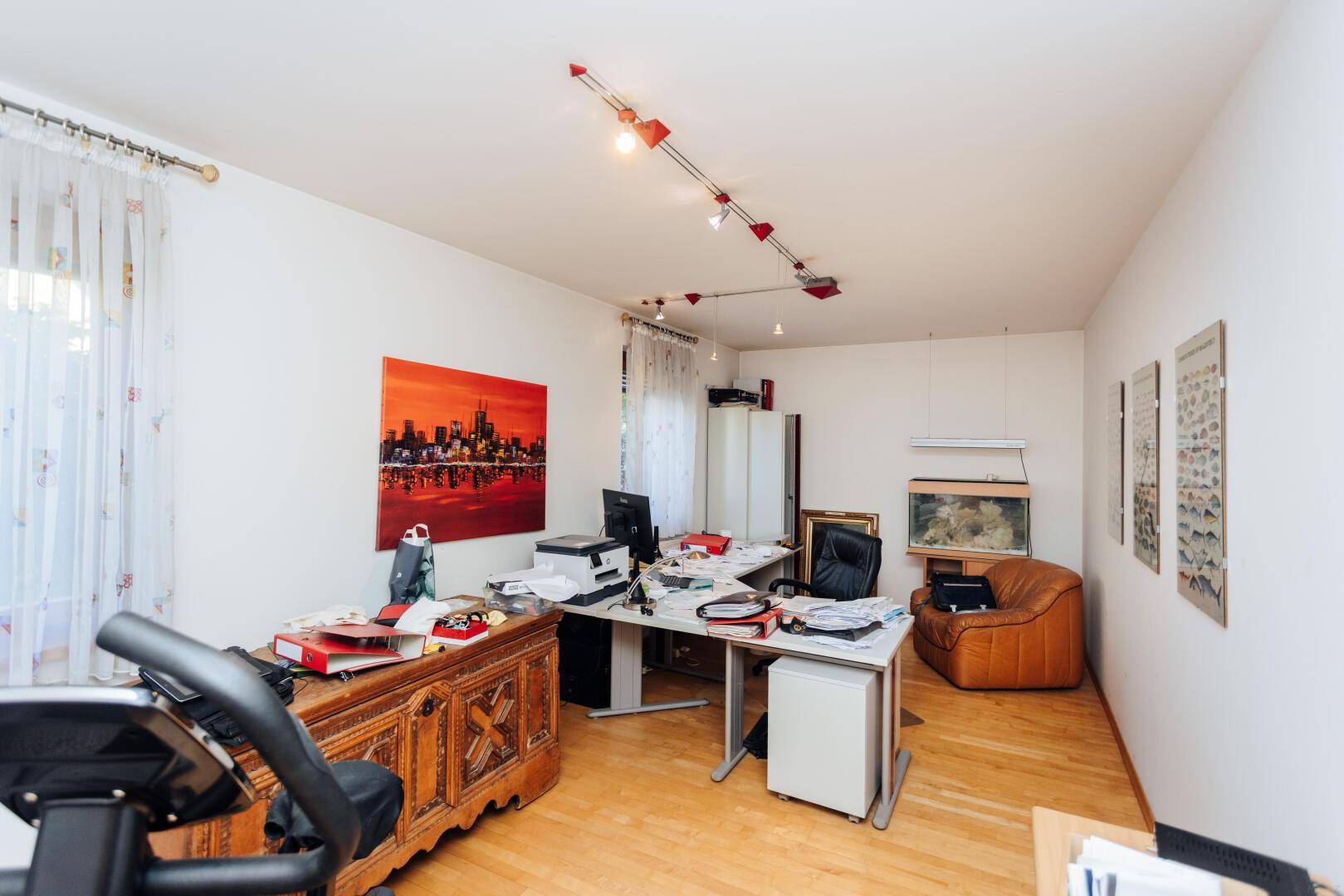 Helles Arbeitszimmer mit Parkettboden, Schreibtisch und einem Aquarium.