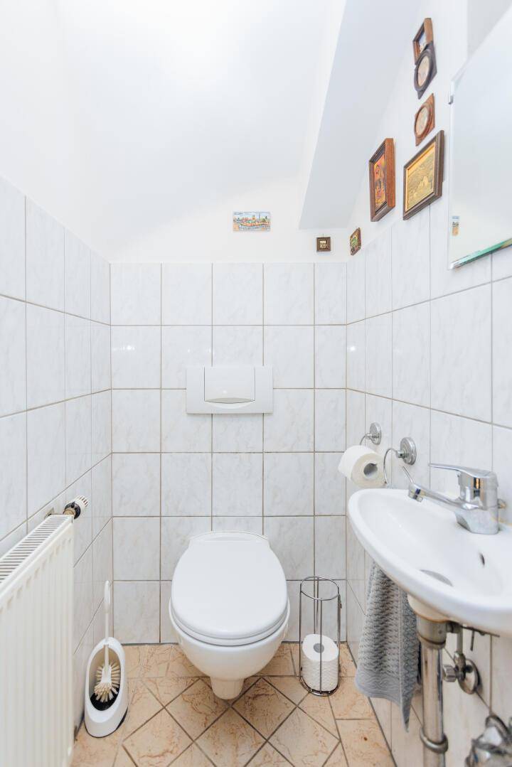 Separate Toilette mit Waschbecken und Fliesen an Wänden und Boden.