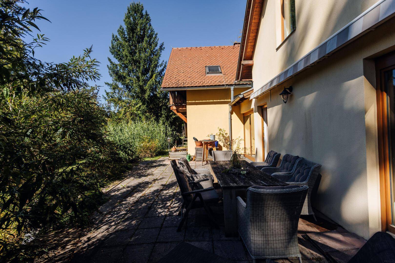 Gemütliche Terrasse mit großem Esstisch und Stühlen, umgeben von Pflanzen.