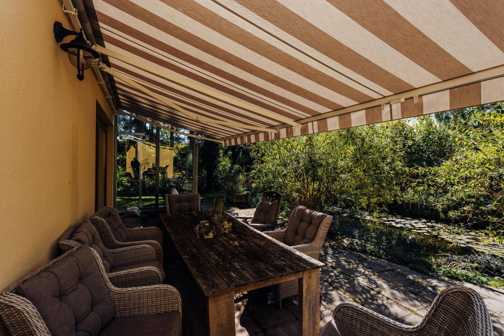 Überdachte Terrasse mit Esstisch und Blick auf den Gartenteich.