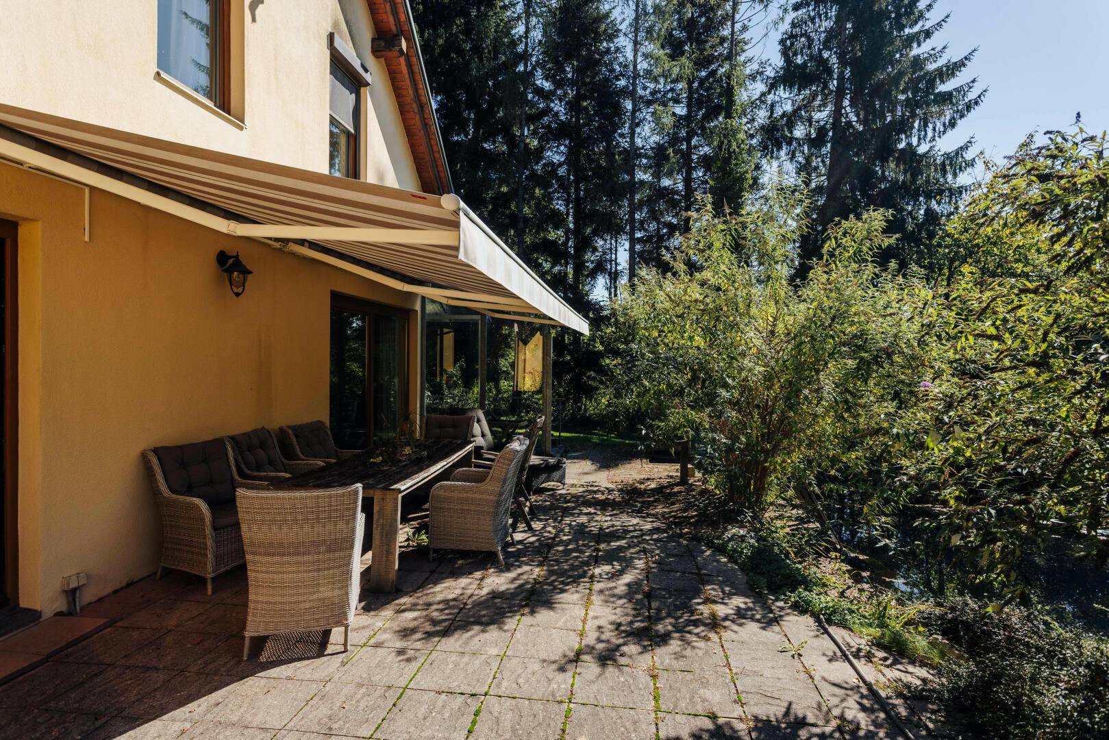 Sonnige Terrasse mit Markise und Gartenmöbeln, ideal für Mahlzeiten im Freien.