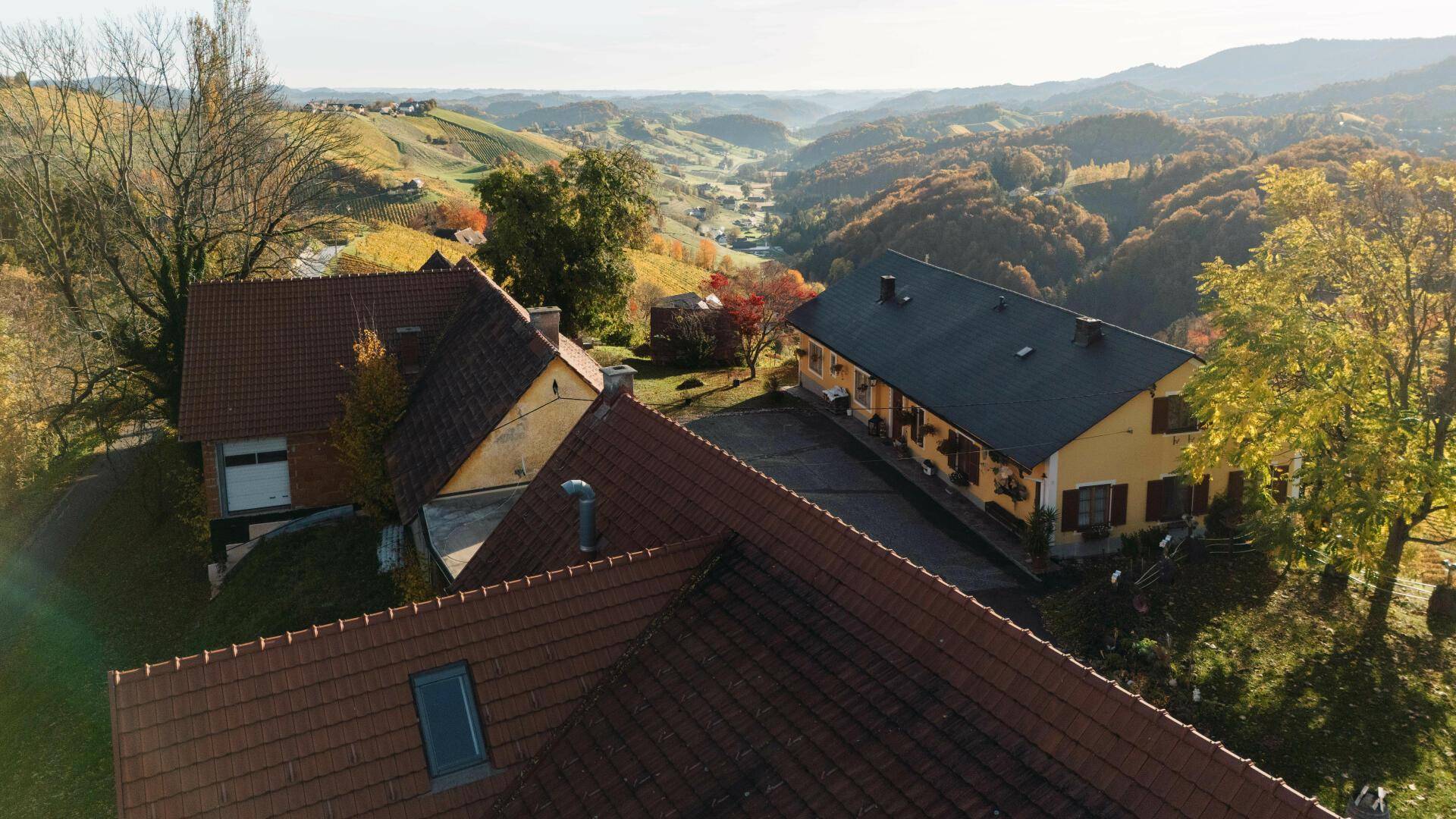 Anwesen mit traditionellen Ziegeldächern und einem Dachfenster, eingebettet in die herbstliche Hügellandschaft.