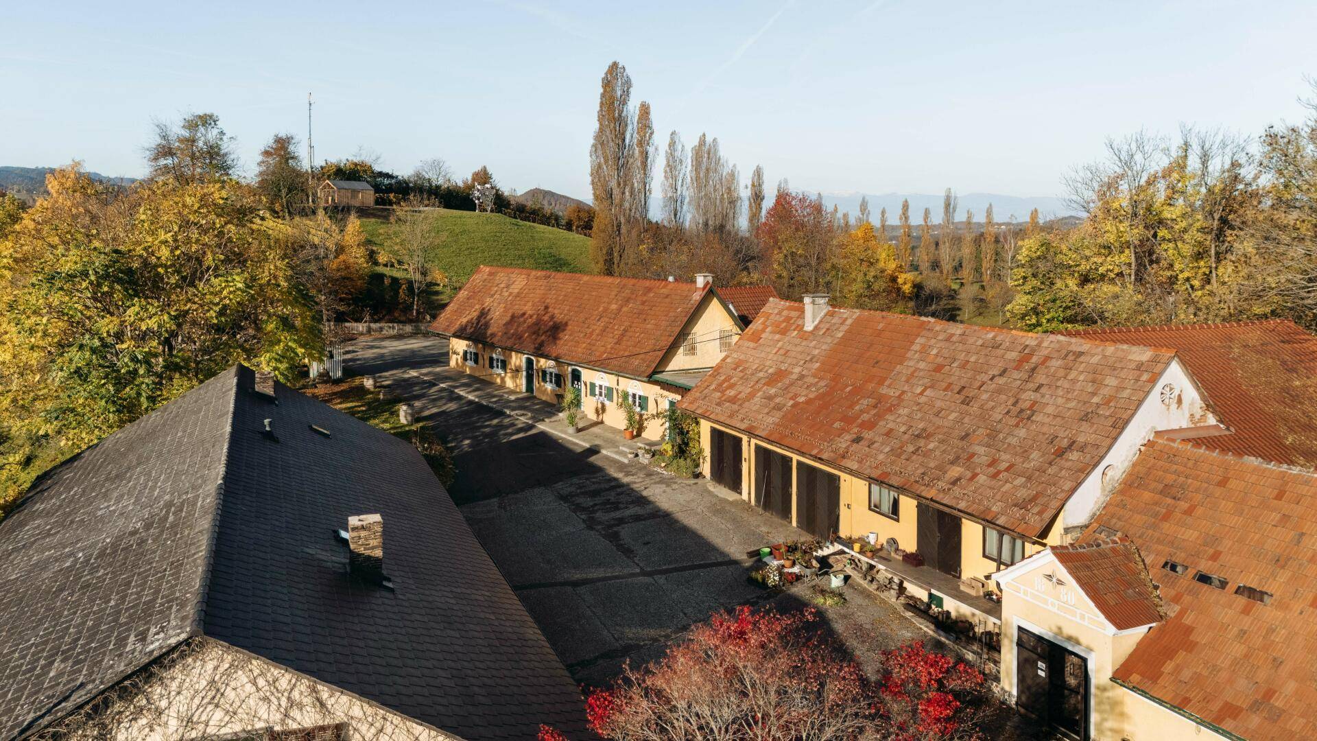 Dachansicht der traditionellen Gebäude mit Ziegeldächern und Innenhof, umgeben von herbstlicher Natur.
