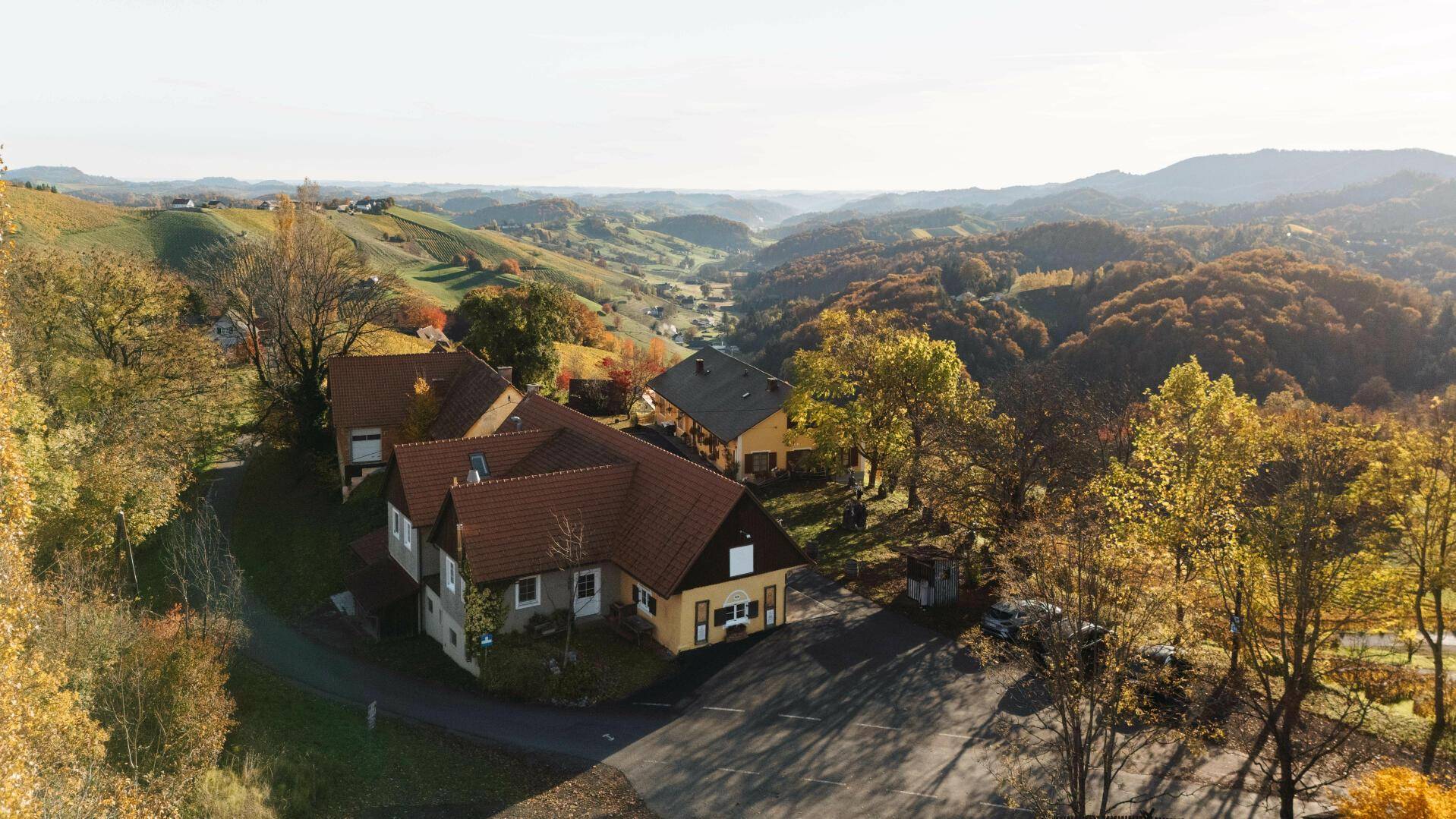 Anwesen mit mehreren Gebäuden und Parkplätzen, umgeben von herbstlichen Bäumen und einer weiten Hügellandschaft.