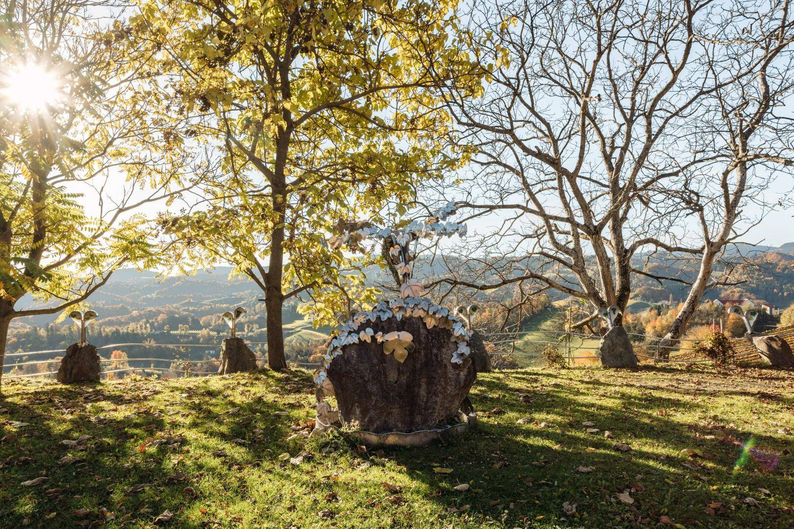 Künstlerische Skulptur in einer grünen Hügellandschaft unter strahlendem Sonnenschein.